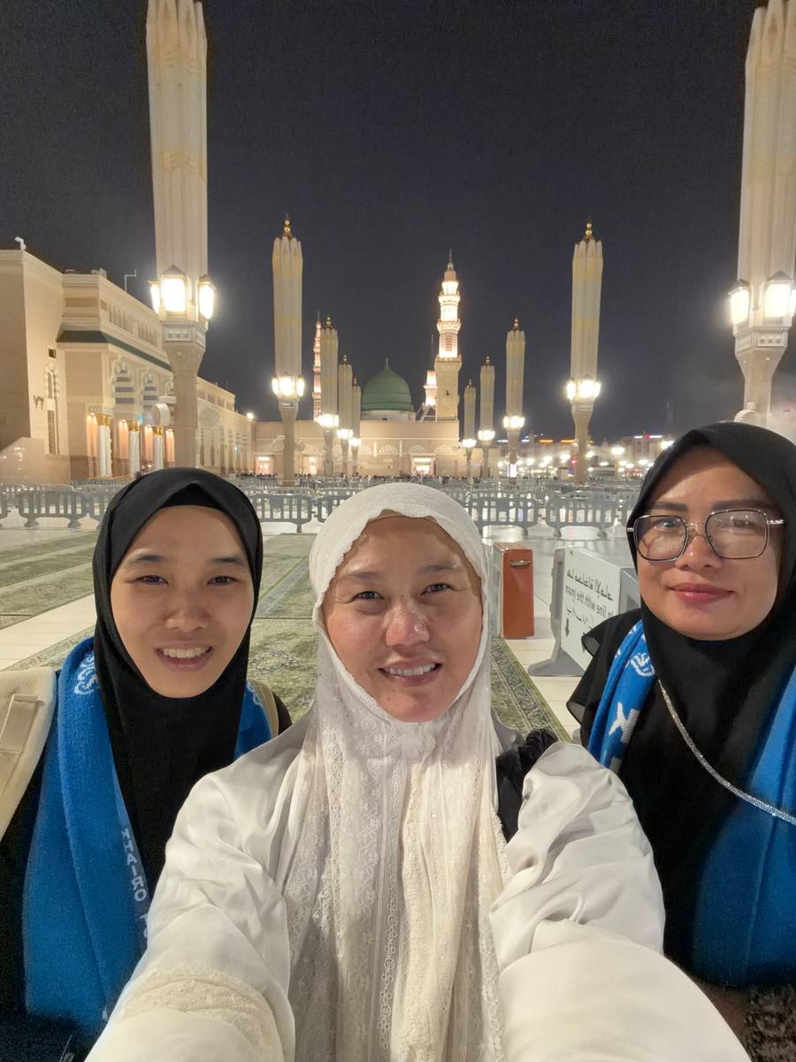 Jamaah berfoto di malam hari dengan Masjid Nabawi yang diterangi lampu