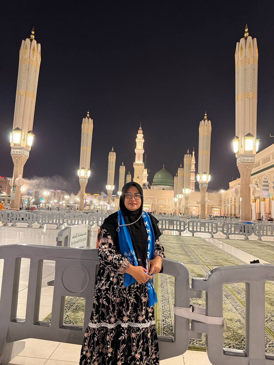 Jamaah di area taman Masjid Nabawi pada malam hari dengan menara menerangi langit